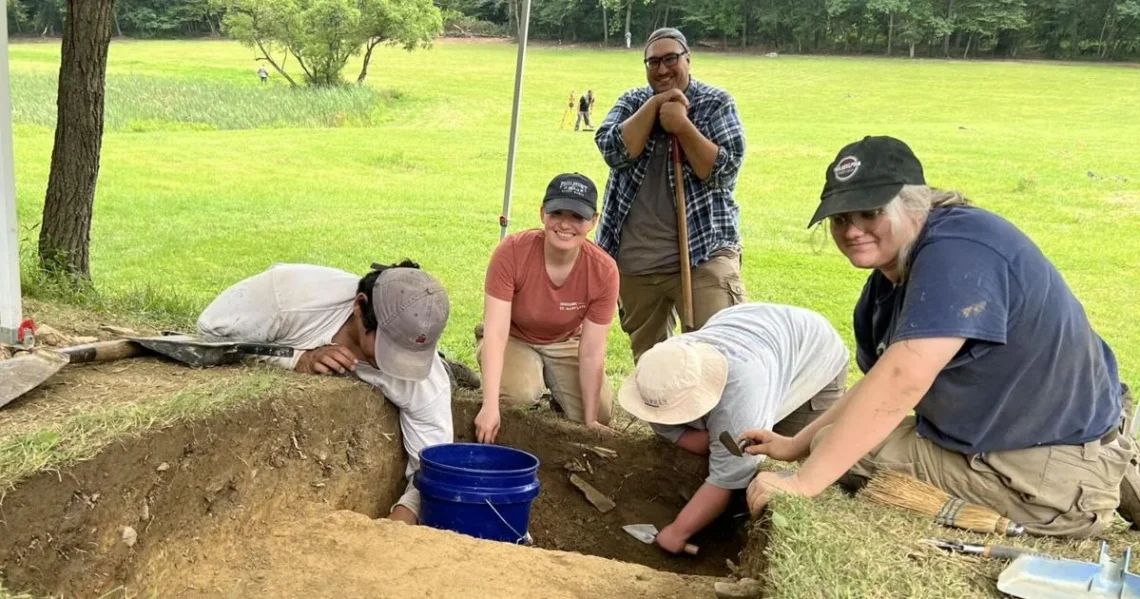 Archaeologists search a grassy battlefield near Fort Ligonier with metal detectors and excavation tools