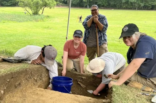 Archaeologists search a grassy battlefield near Fort Ligonier with metal detectors and excavation tools
